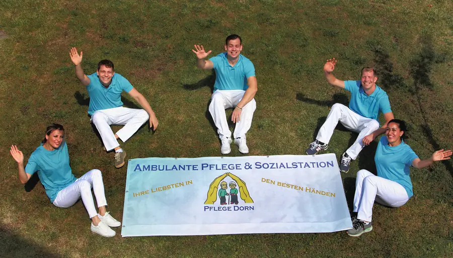 Das Team von Pflege Dorn von oben fotografiert, im Kreis auf der Wiese um das Banner mit dem Logo